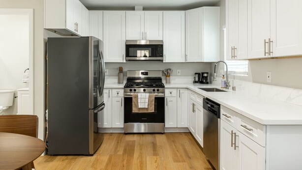 A modern kitchen with white cabinets, stainless steel appliances, and a wooden floor.