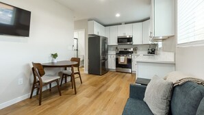 A modern kitchen with white cabinets, stainless steel appliances, and a dining area with wooden furniture.