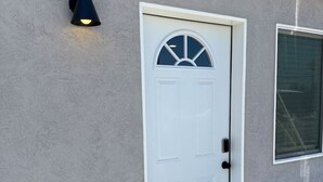 A white door with a semi-circular window above it, a small wall-mounted light fixture to the left, and a window to the right.