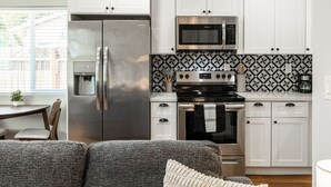 Une cuisine moderne dotée d’appareils électroménagers en acier inoxydable, de meubles blancs et d’un revêtement mural décoratif.