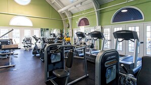 Une salle de sport équipée de divers appareils d’exercice, dotée de grandes fenêtres et d’un plafond haut.