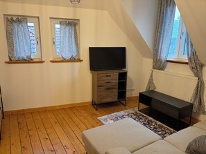 Ein Schlafzimmer mit einem Bett, einem Fernseher auf einem Schrank, einer Kommode und zwei mit Vorhängen versehenen Fenstern.