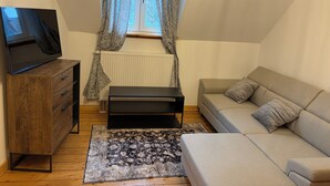 Une petite pièce chaleureuse, avec une commode en bois, un pouf noir, un canapé beige et un tapis à motifs.