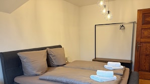 Une chambre à coucher avec un lit, des oreillers, une table de chevet, une lampe, un miroir et une porte en bois.