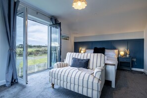 A room with a bed, a sofa, a bedside table, and a window with a view of the outdoors. - Ty Wawr: Spacious 3-Bedroom Holiday Home, Anglesey (Brynteg)
