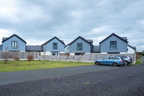 A row of blue houses with a gravel driveway and a parked car. - Ty Wawr: Spacious 3-Bedroom Holiday Home, Anglesey (Brynteg)