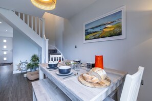 A dining area with a wooden table, chairs, and a painting on the wall. - Ty Wawr: Spacious 3-Bedroom Holiday Home, Anglesey (Brynteg)