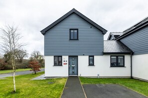 Um edifício residencial de dois andares com telhado cinzento, porta de entrada central e uma pequena janela no andar de cima.