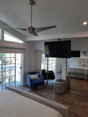 A spacious room with a ceiling fan, a large flat-screen TV, a bed, and a seating area with two chairs. - DP Lantern District Townhouse STR-23-0105 (Dana Point)