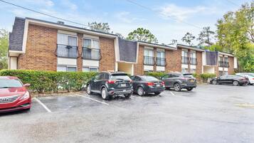 Uma fileira de edifícios de apartamentos modernos de tijolo com varandas, um estacionamento com vários carros e um céu limpo.