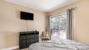 Un dormitorio con una cama, un tocador, una silla, un televisor y una ventana con cortinas.