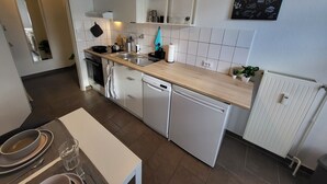 Eine moderne Küche mit weißen Schränken, einer Holzarbeitsplatte und einem eingebauten Geschirrspüler. Es gibt eine kleine Essecke mit einem Tisch für zwei Personen.