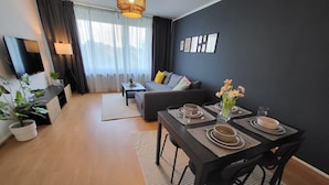 Ein modernes Wohnzimmer mit Essbereich, ausgestattet mit einer Couch, einem Fernseher und einem Esstisch, gedeckt mit Tellern und Gläsern.