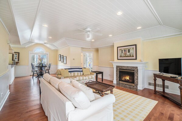 A spacious living room with a white sofa, a fireplace, a television, and a dining area with a table and chairs. - Downtown! Above local businesses and walking distance to everything! (Harbor Springs)