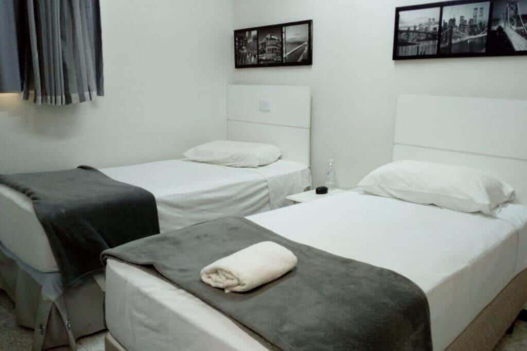 A hotel room with two single beds, a gray blanket on the floor, and black-and-white cityscape pictures on the wall.