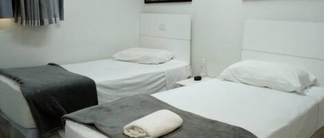 A hotel room with two single beds, a gray blanket on the floor, and black-and-white cityscape pictures on the wall.