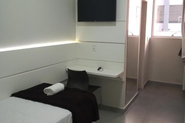 Une chambre d’hôtel de taille réduite, comprenant un lit, un petit bureau, une chaise et un téléviseur fixé au mur.