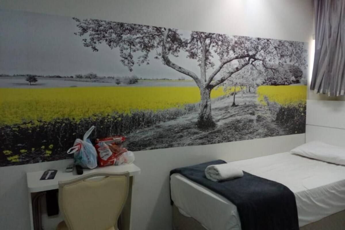A hotel room with a bed, a desk, and a large wall mural depicting a tree and a field.