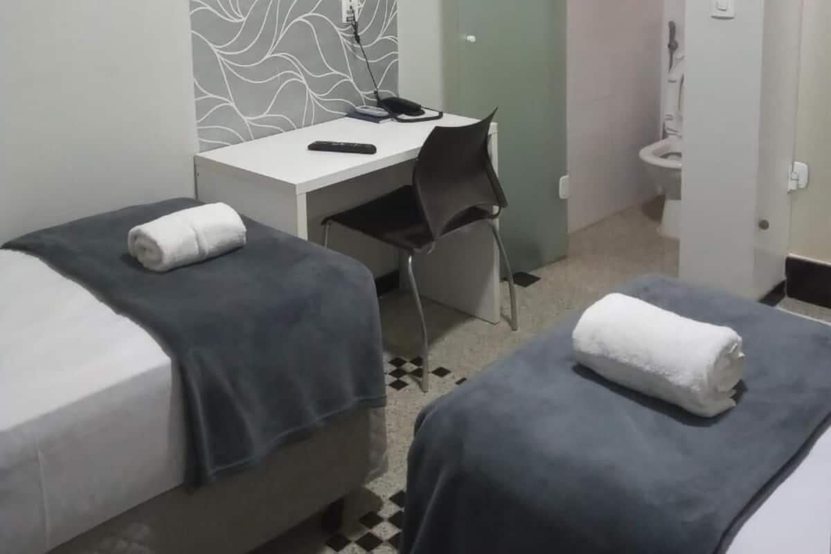 A hotel room with two beds, a desk, a chair, and a toilet.