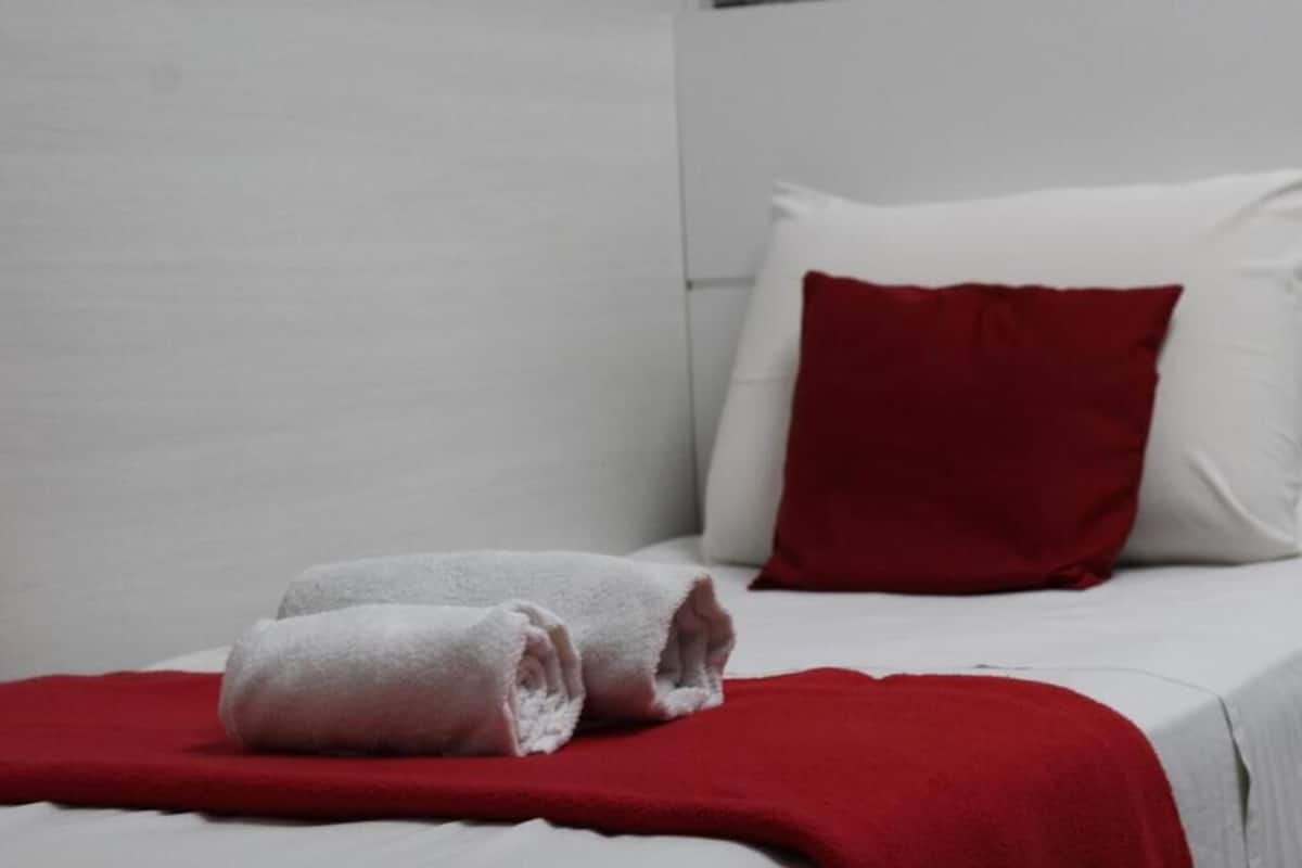 A neatly made bed with white bedding and a red throw blanket.