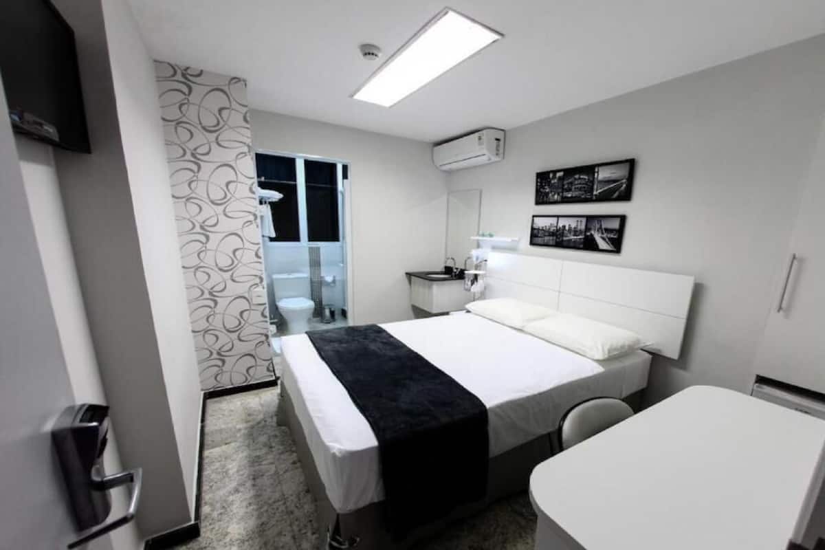 A hotel room with a bed, a desk, a chair, a bathroom, and a shower.