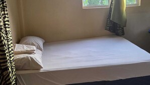 A single bed with white bedding, a window with a zebra-patterned curtain, and a plain wall. - Adorable 3-bedroom apartment with AC in Elms Hall Roseau. (Elms Hall, Roseau)
