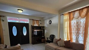 A spacious living room with a sofa set, a television, and a dining area with a table and chairs. - Adorable 3-bedroom apartment with AC in Elms Hall Roseau. (Elms Hall, Roseau)