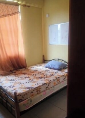 A small, single-bed room with a floral bedspread, a single pillow, and a whiteboard on the wall. - Adorable 3-bedroom apartment with AC in Elms Hall Roseau. (Elms Hall, Roseau)