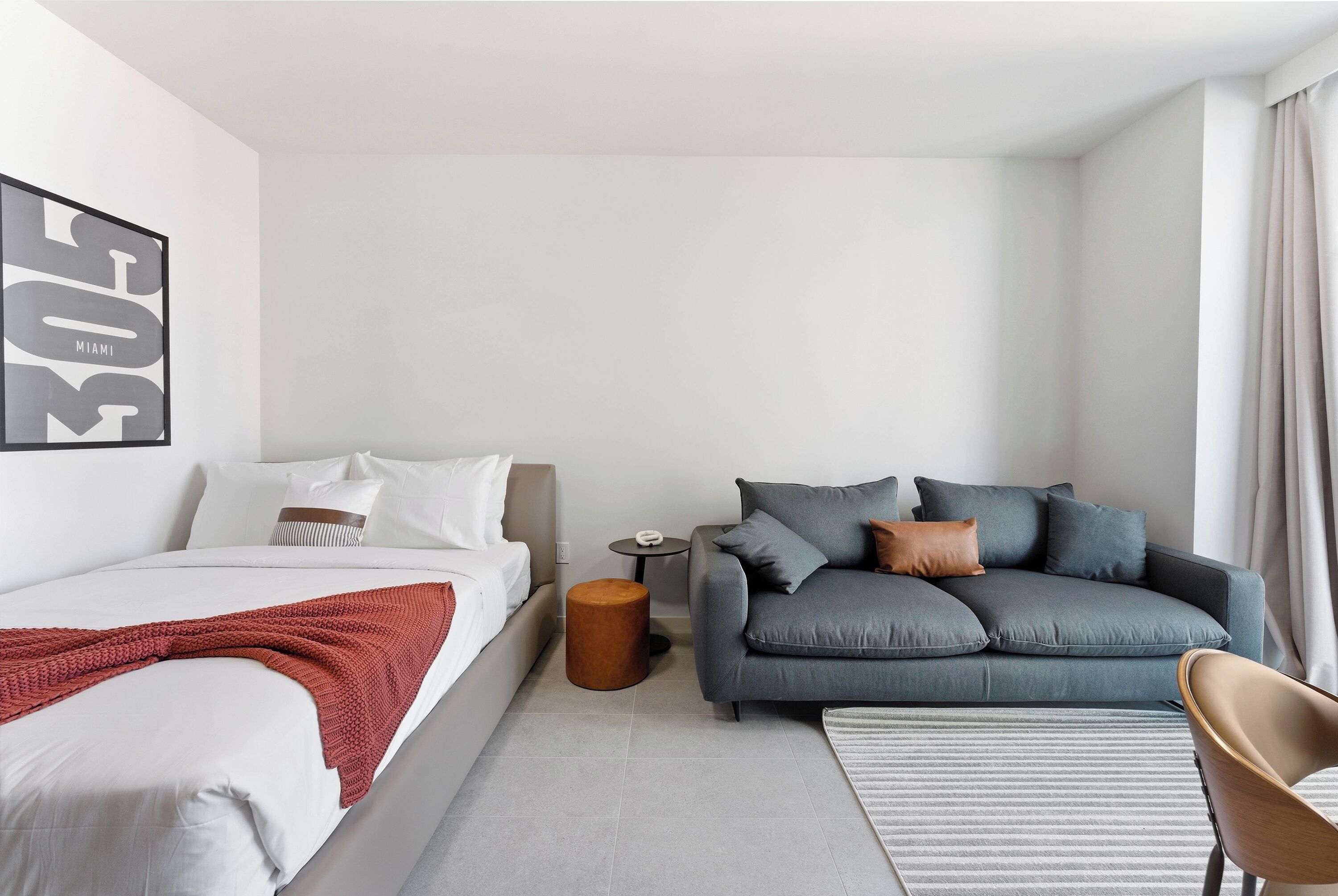 Una habitación de hotel moderna con una cama, un sofá gris, una mesita redonda y una silla.