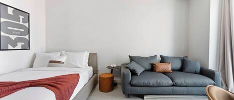 Una habitación de hotel moderna con una cama, un sofá gris, una mesita redonda y una silla.