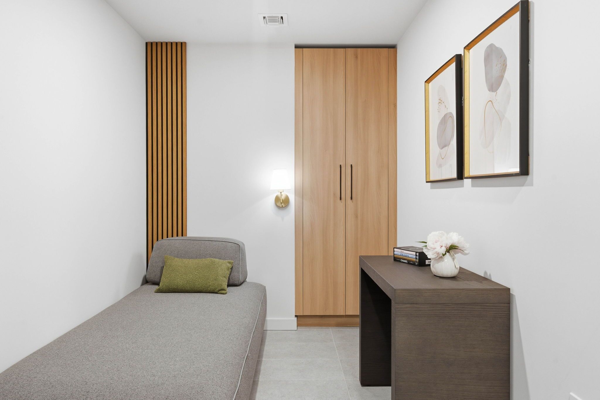 Une chambre  à coucher moderne avec un lit, une armoire en bois, une table de chevet et des œuvres d’art encadrées accrochées au mur.
