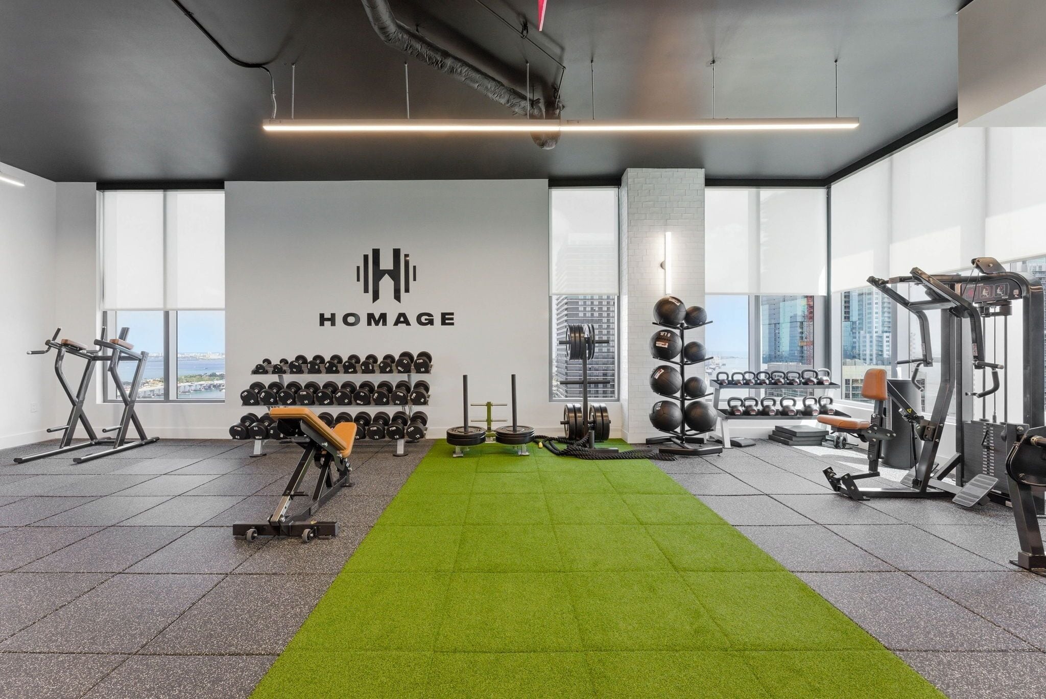 A gym with a green carpet, weightlifting equipment, and dumbbells.