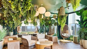 A modern living room with a high ceiling, wooden flooring, and a variety of plants and greenery. There are comfortable seating areas, including a sofa and chairs, and a round coffee table. - 501 First Residences (Miami)
