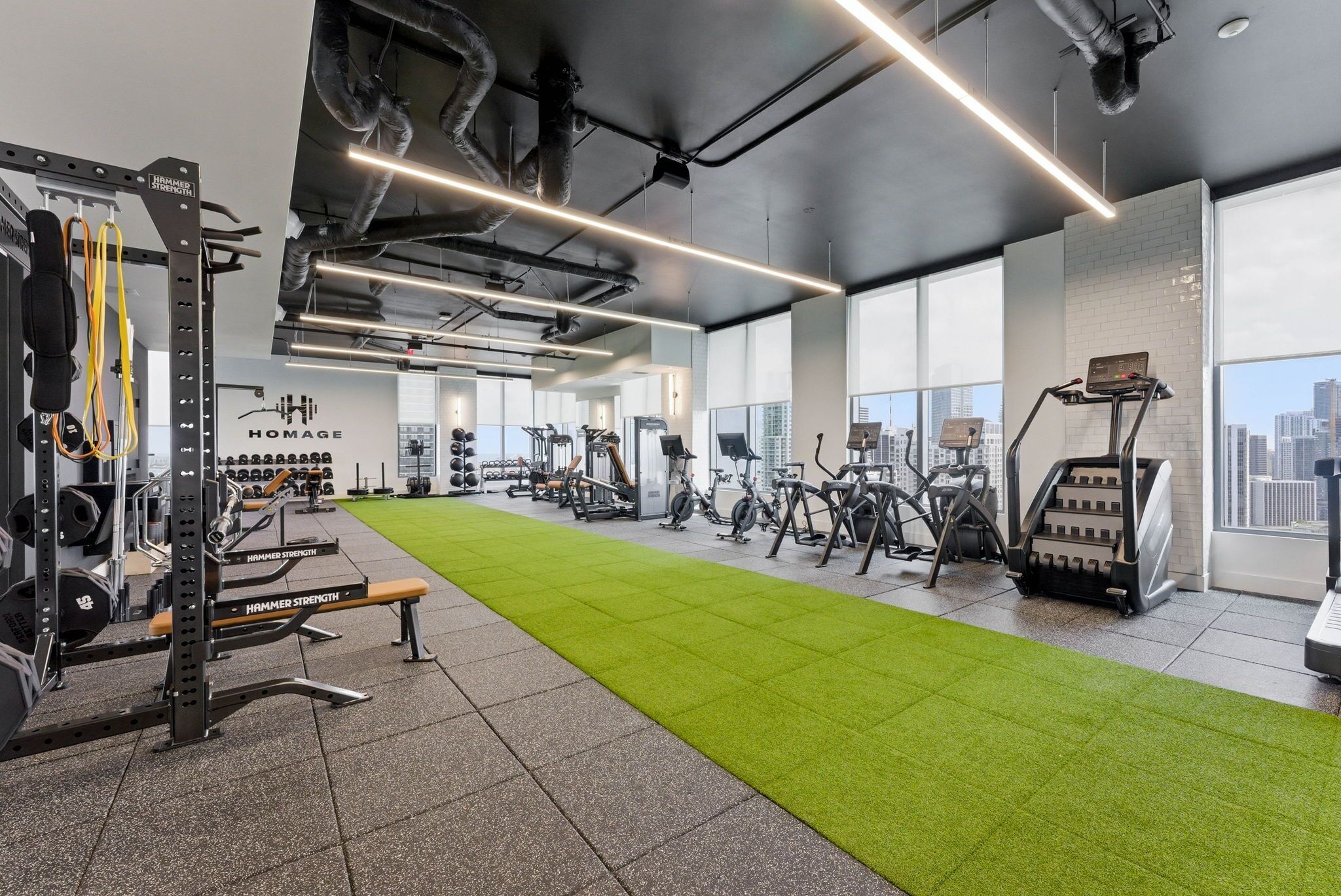 A gym with exercise equipment, a green exercise mat, and a city view through large windows.