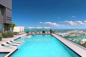 Una piscina infinita en la azotea con sillones y sombrillas, con vistas a una ciudad costera.