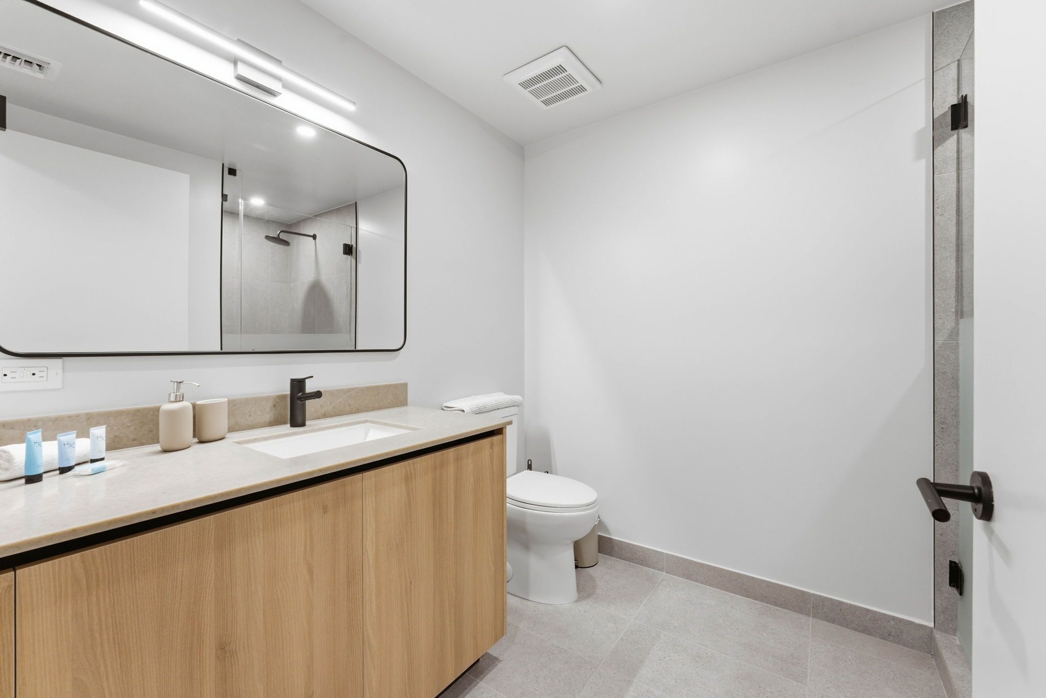 A modern bathroom with a large mirror, two sinks, a toilet, and a shower area.