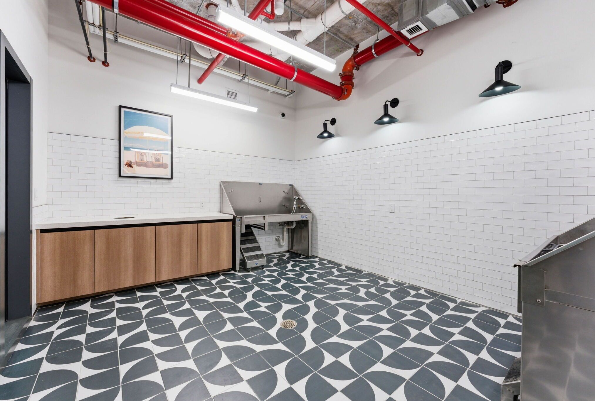 A modern kitchen with a geometric tile floor, white brick walls, and red and black pendant lights.