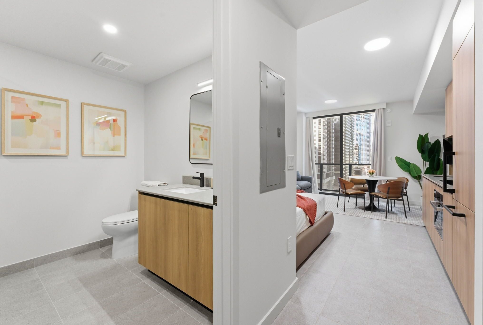 A modern bathroom with a toilet, sink, and cabinet. There is a dining area with a table and chairs.