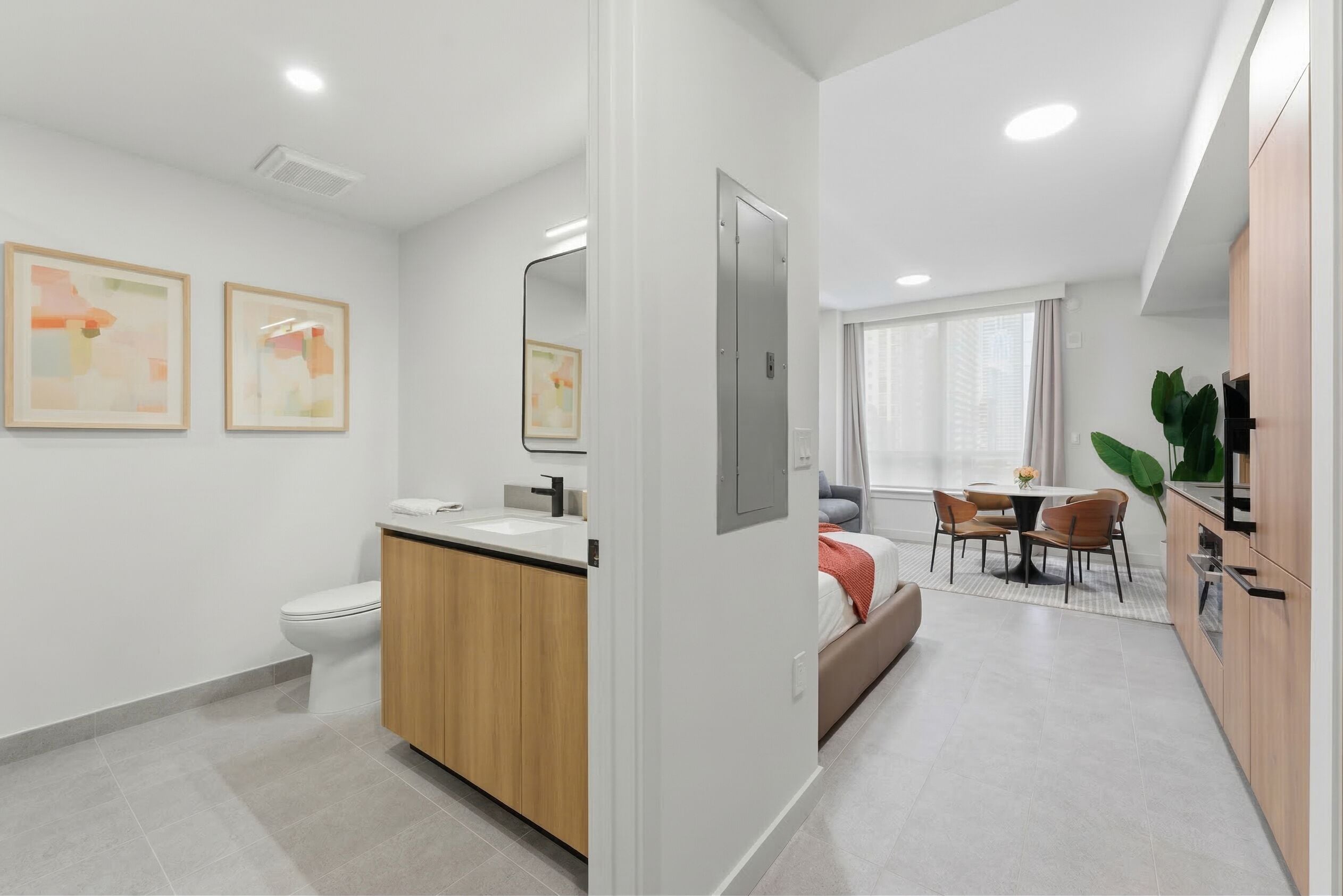 Une salle de bain moderne comprenant des toilettes, un lavabo et un meuble de rangement, un coin repas avec une table et des chaises, et une cuisine avec des placards et une plante.
