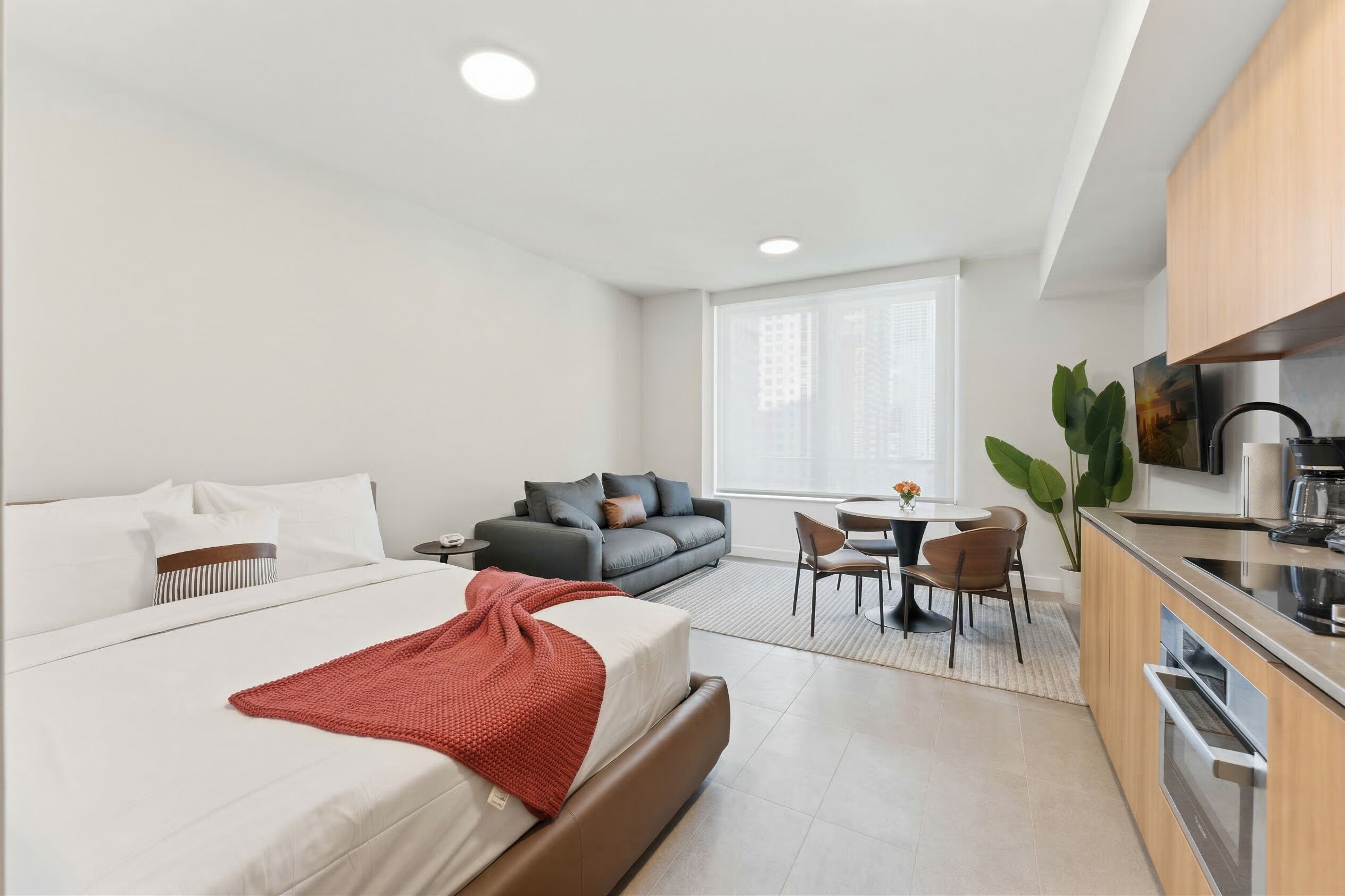 Een moderne hotelkamer met een bed, een bank, een eethoek en een kitchenette.