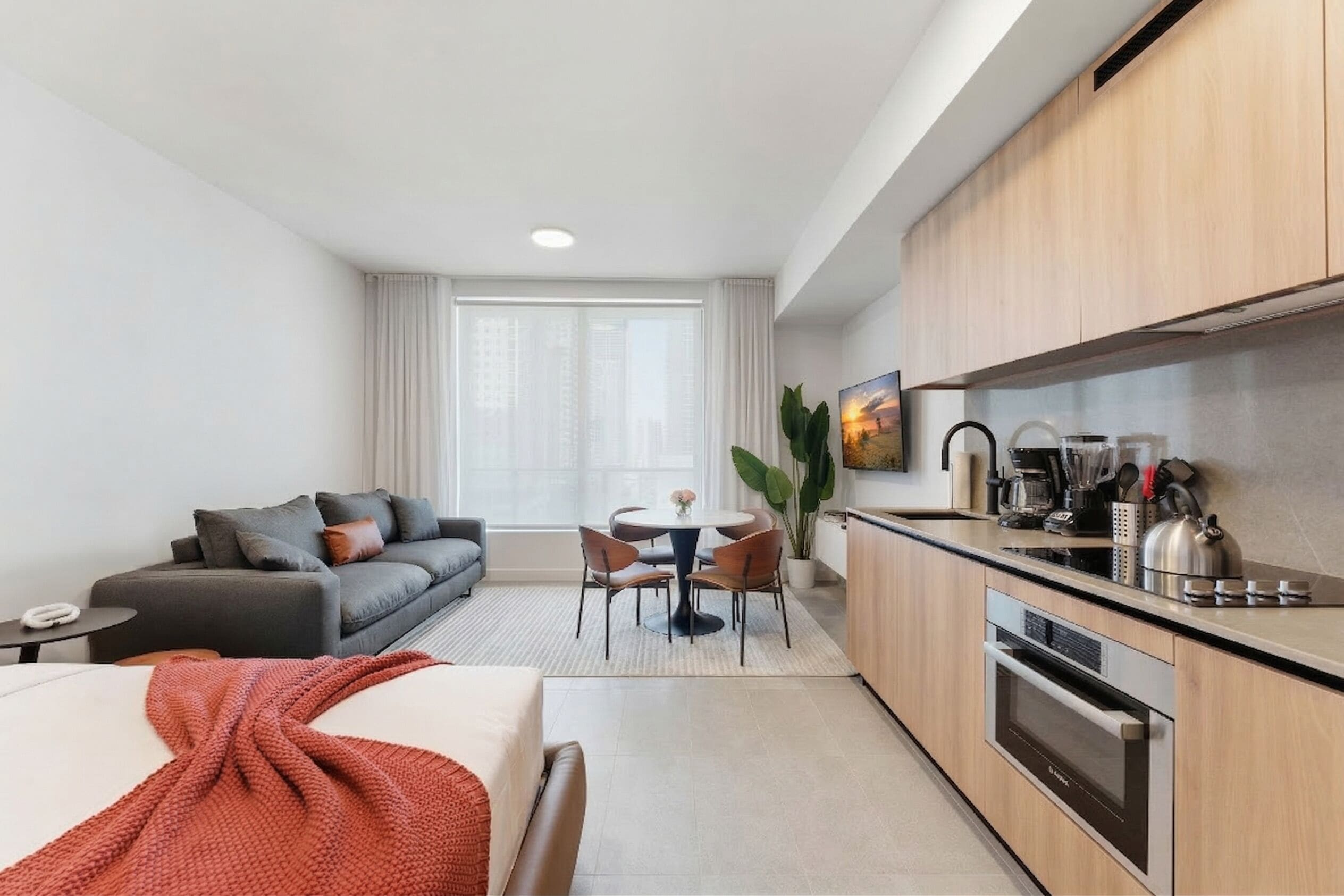 A modern hotel room with a sofa, dining table, and kitchenette.