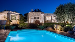 Une maison moderne dotée d’une piscine, d’une façade en pierre et d’un éclairage extérieur.