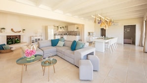 Un vaste espace de vie comprenant un grand canapé en forme de L, une table basse en verre et un coin repas avec une table et des chaises blanches.