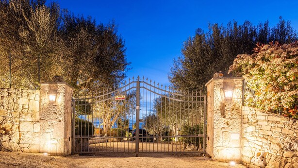 Een poort met stenen muren en een metalen hek, omgeven door bomen en een heldere lucht.