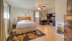 A bedroom with a bed, a ceiling fan, a dresser, and a desk area.