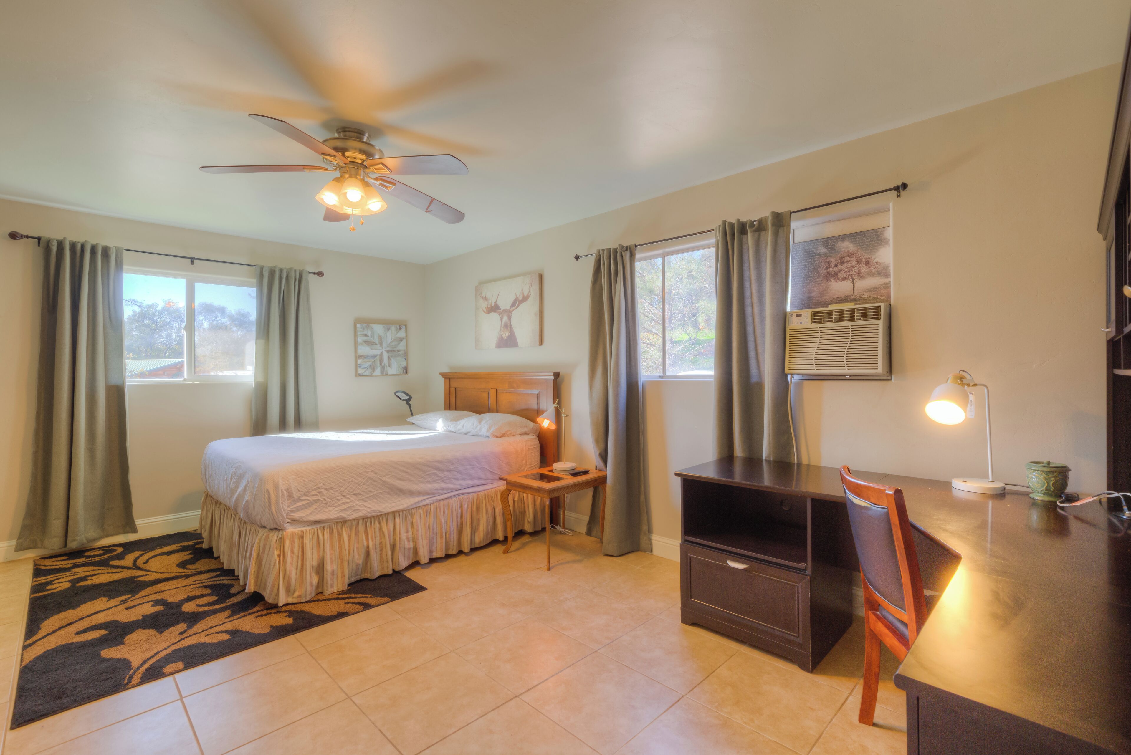 A bedroom with a bed, a desk, a chair, a ceiling fan, and a window with curtains.