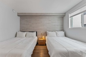 Ein Schlafzimmer mit zwei Betten, einem Nachttisch mit Lampe und einem Fenster mit Jalousien.