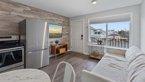 A modern kitchen with stainless steel appliances, a dining area with a marble table, and a balcony with a view of houses. - 1BR Condo 1 Block from the Beach & Boardwalk (Wildwood)
