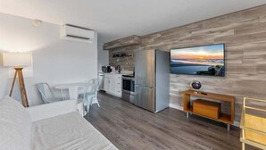 A modern room with a bed, a desk, a chair, a TV, a kitchen area, and a wooden wall. - 1BR Condo 1 Block from the Beach & Boardwalk (Wildwood)