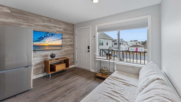 A modern kitchen with a refrigerator, a wooden cabinet, and a dining area with a table and chairs. - 1BR Condo 1 Block from the Beach & Boardwalk (Wildwood)